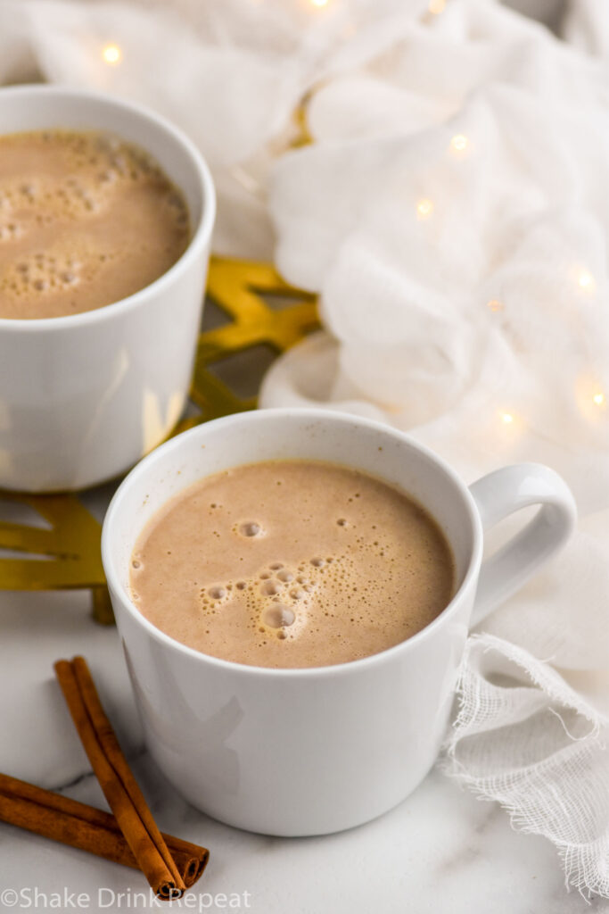 two mugs of Spiked Eggnog Latte surrounded by cinnamon sticks
