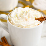 mug of Spiked Eggnog Latte recipe topped with whipped cream and a cinnamon stick