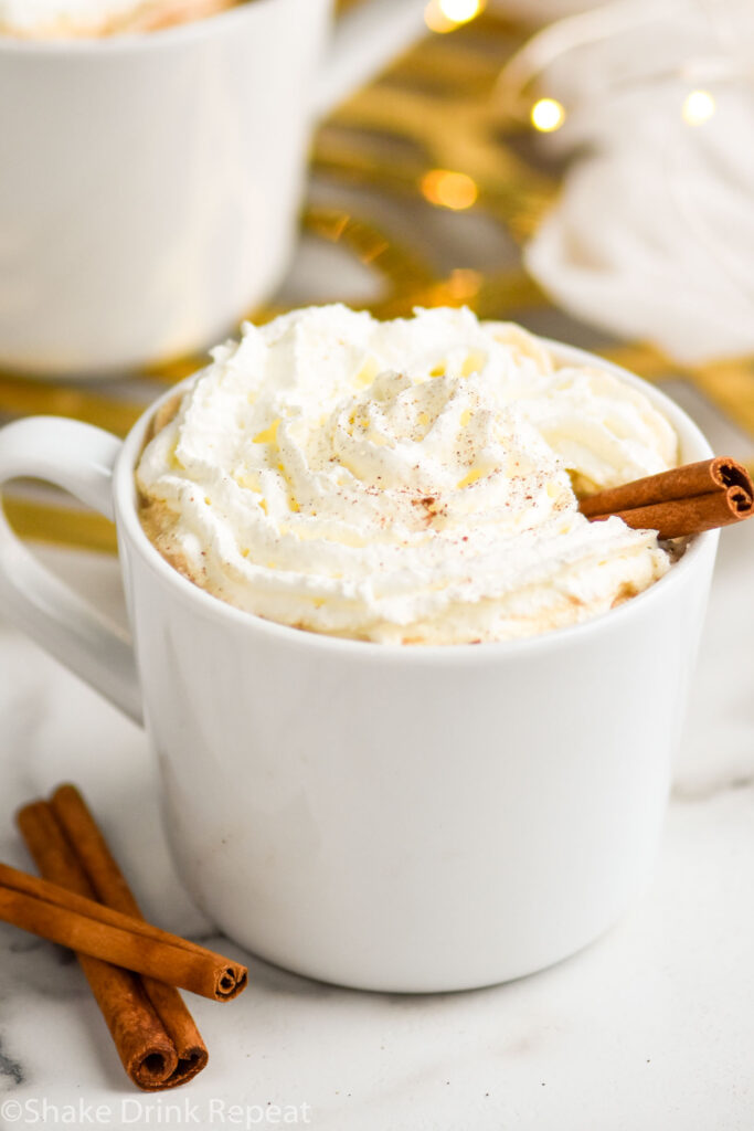 mug of Spiked Eggnog Latte recipe topped with whipped cream and a cinnamon stick