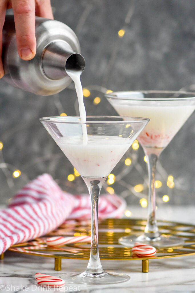 man's hand pouring cocktail shaker of Candy Cane Martini recipe into a martini glass with crushed candy canes