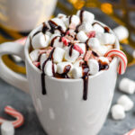 two mugs of boozy peppermint hot chocolate garnished with marshmallows, chocolate drizzle, and candy canes