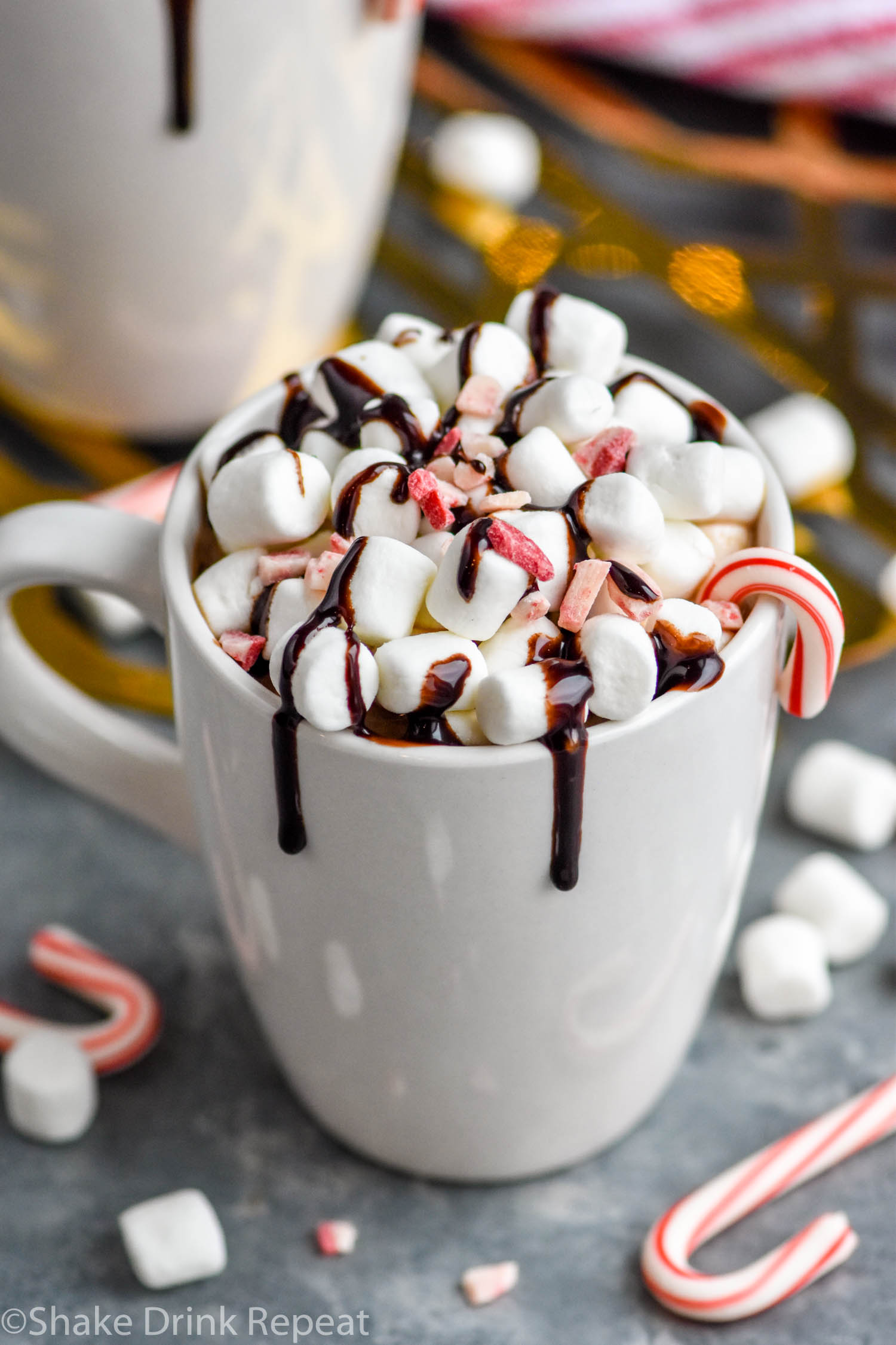 two mugs of boozy peppermint hot chocolate garnished with marshmallows, chocolate drizzle, and candy canes