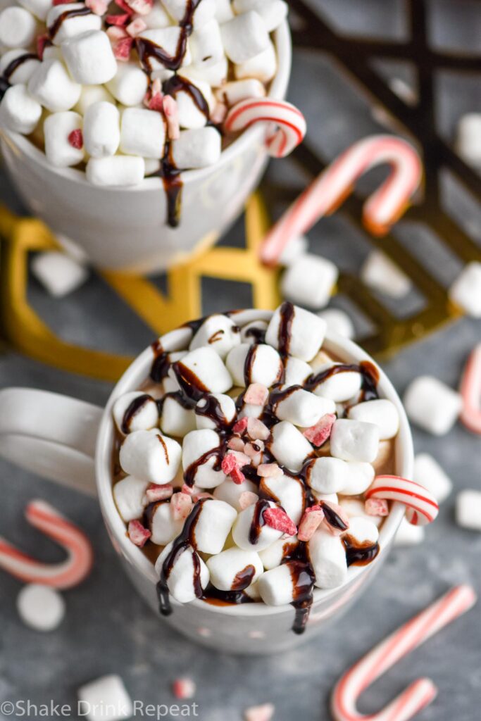 two mugs of boozy peppermint hot chocolate garnished with marshmallows, chocolate drizzle, and candy canes