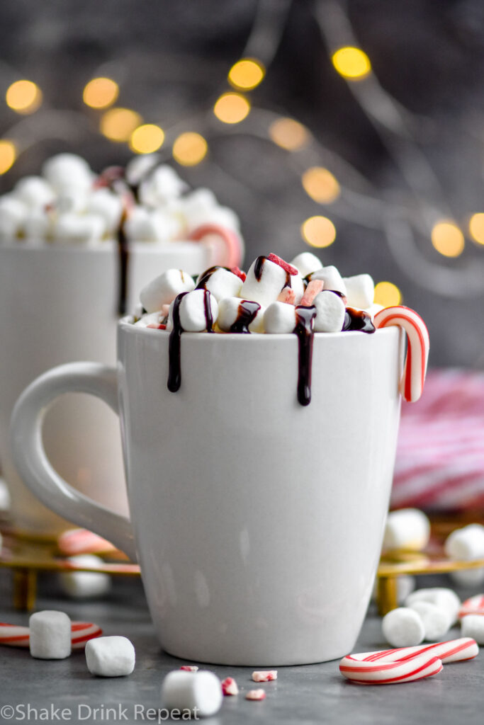 two mugs of boozy peppermint hot chocolate garnished with marshmallows, chocolate drizzle, and candy canes