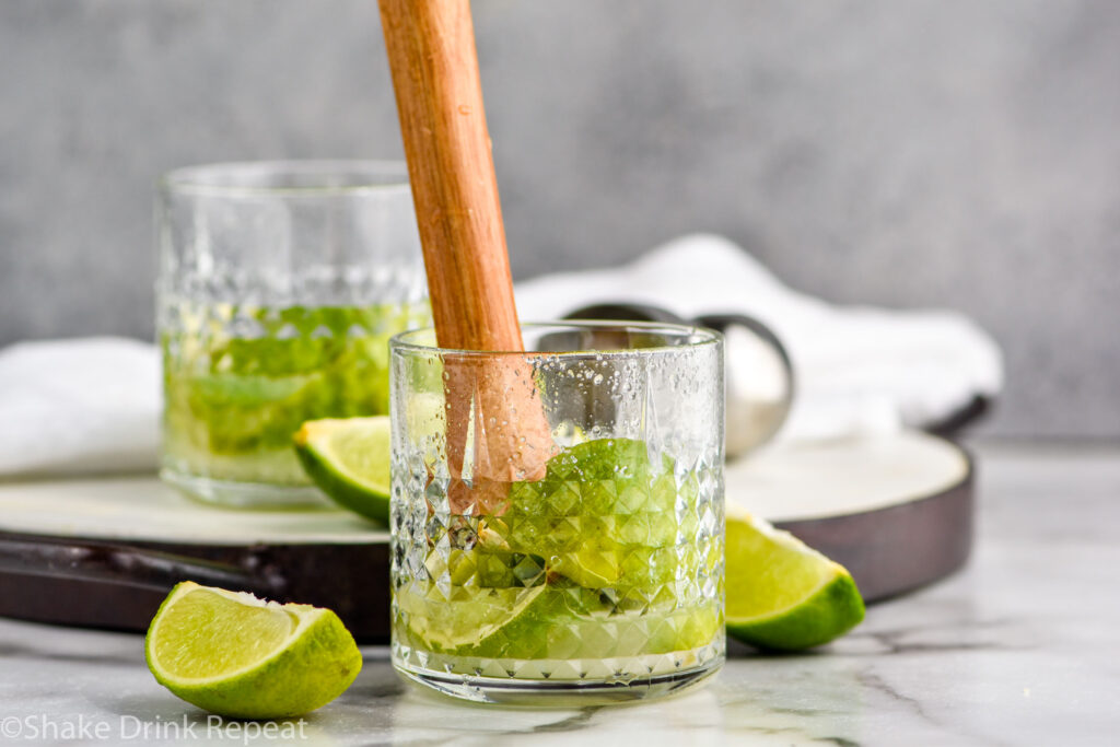 cocktail muddler muddling limes and sugar in a glass to make a Caipiroska recipe