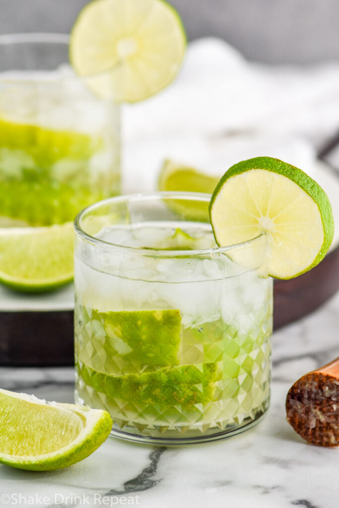 two glasses of Caipiroska recipe with ice garnished with a lime next to a cocktail muddler