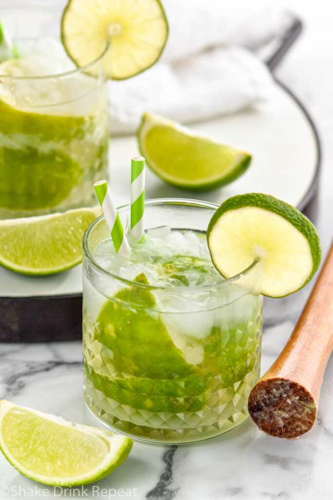 two glasses of Caipiroska recipe with ice garnished with straws and limes