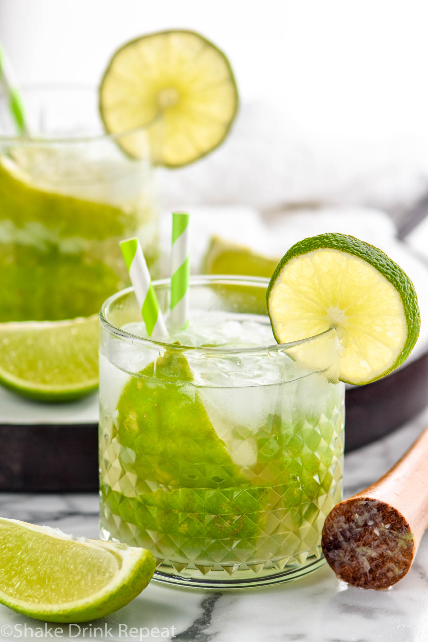 two glasses of Caipiroska recipe with ice garnished with two straws and a lime