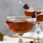 two coupe glasses of Corpse Reviver recipe garnished with Luxardo cherries