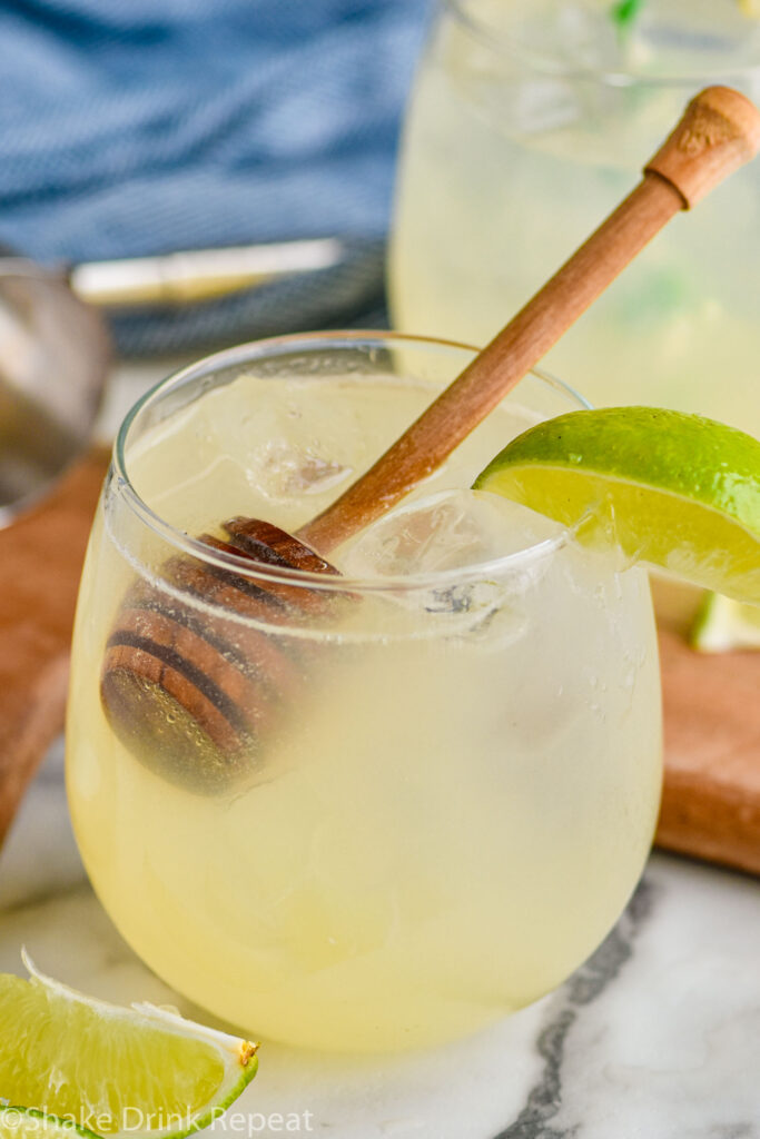 Glass of Canchanchara recipe with ice garnished with a honey dipper and lime wedge