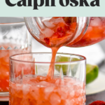 man's hand pouring mason jar of Strawberry Caipiroska ingredients into a glass with crushed ice surrounded by fresh strawberries and lime wedges