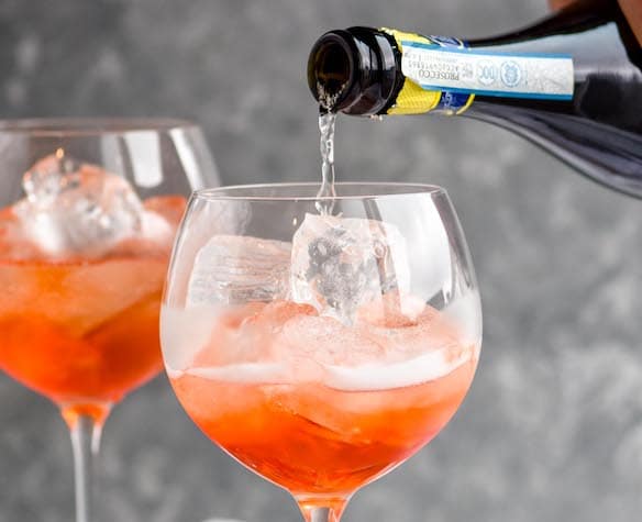 champagne being poured into a wine glass for an aperol spritz