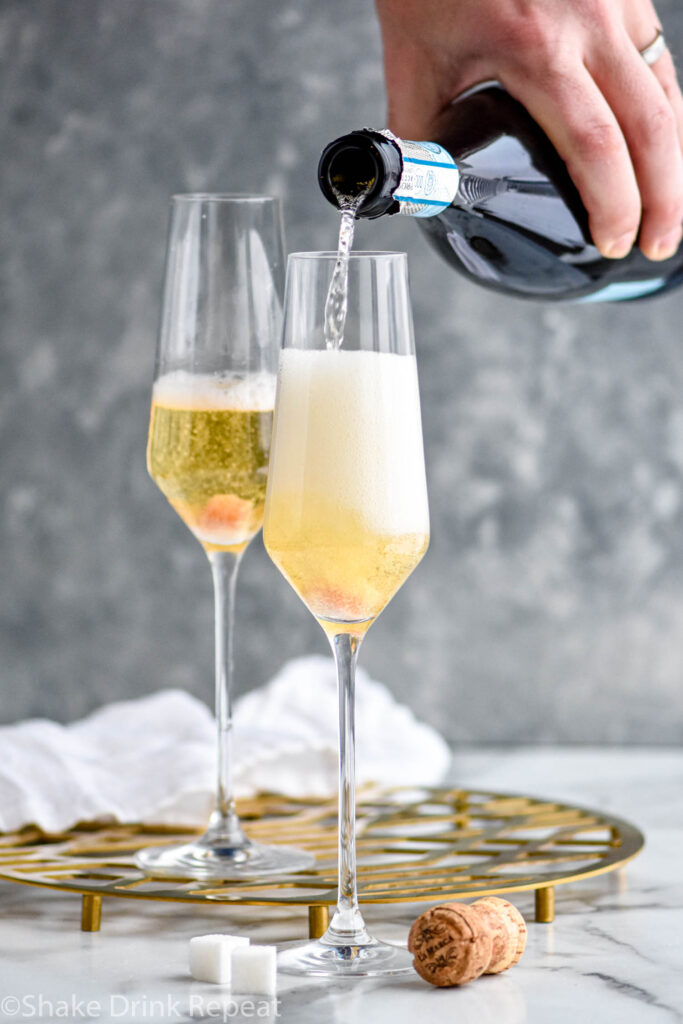 man's hand pouring champagne into a champagne flute of Champagne Cocktail ingredients