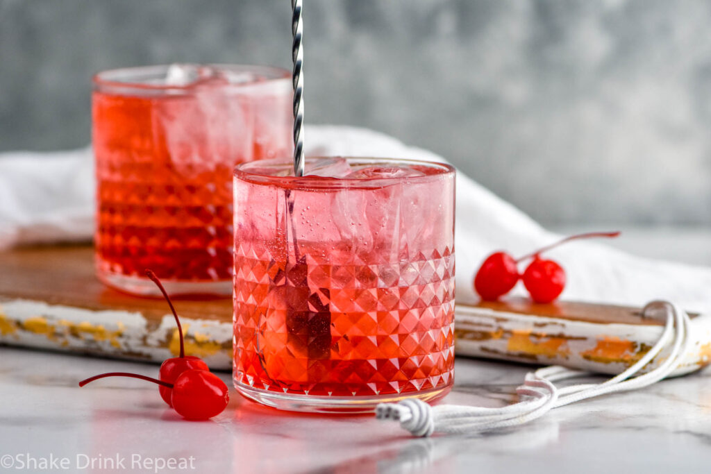 stir stick stirring glass of Dirty Shirley drink recipe surrounded by maraschino cherries