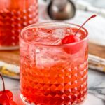 Two glasses of Dirty Shirley drinks with ice and maraschino cherries