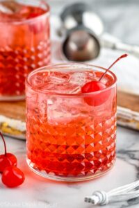 Two glasses of Dirty Shirley drinks with ice and maraschino cherries