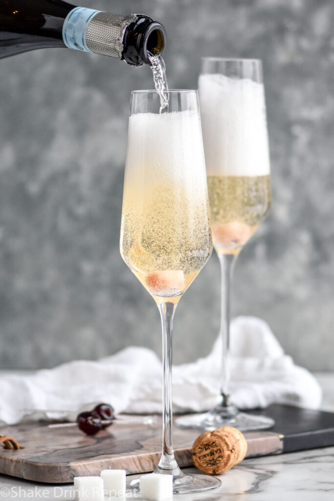 bottle of champagne pouring into two champagne flutes of Gin Champagne Cocktail