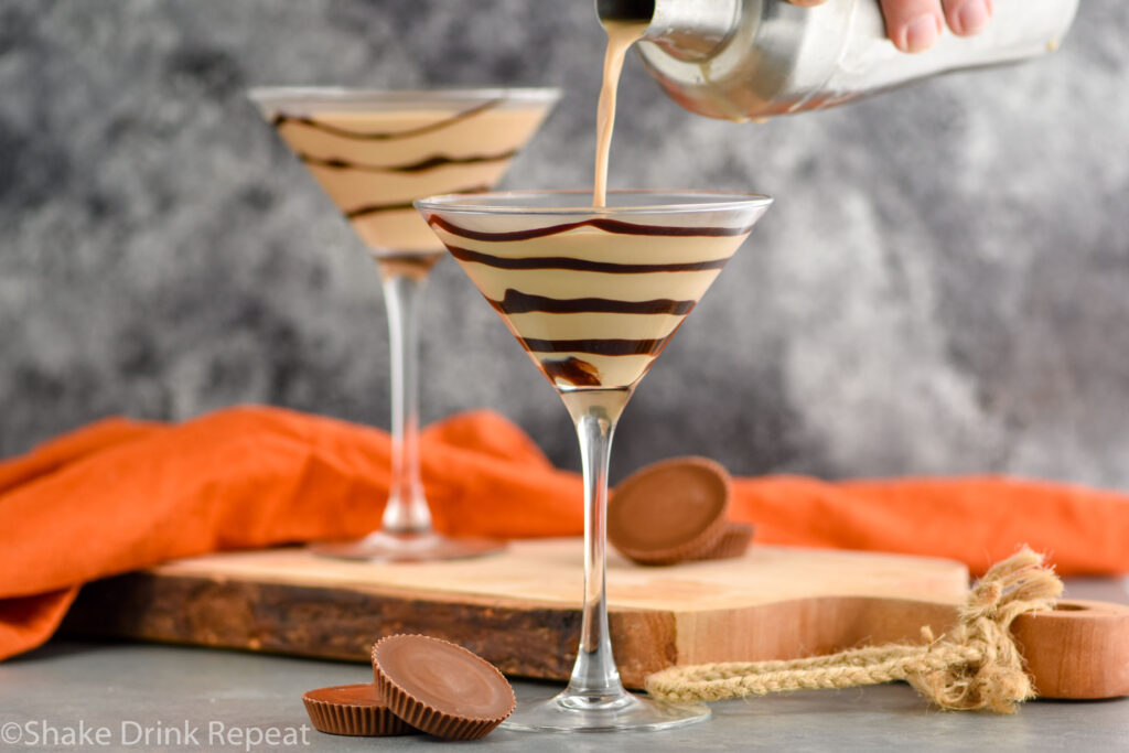 man's hand pouring cocktail shaker of Peanut Butter Cup Martini ingredients into a martini glass drizzled with chocolate