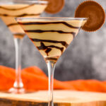 two martini glasses of Peanut Butter Cup Martini recipe garnished with chocolate drizzle and a peanut butter cup.