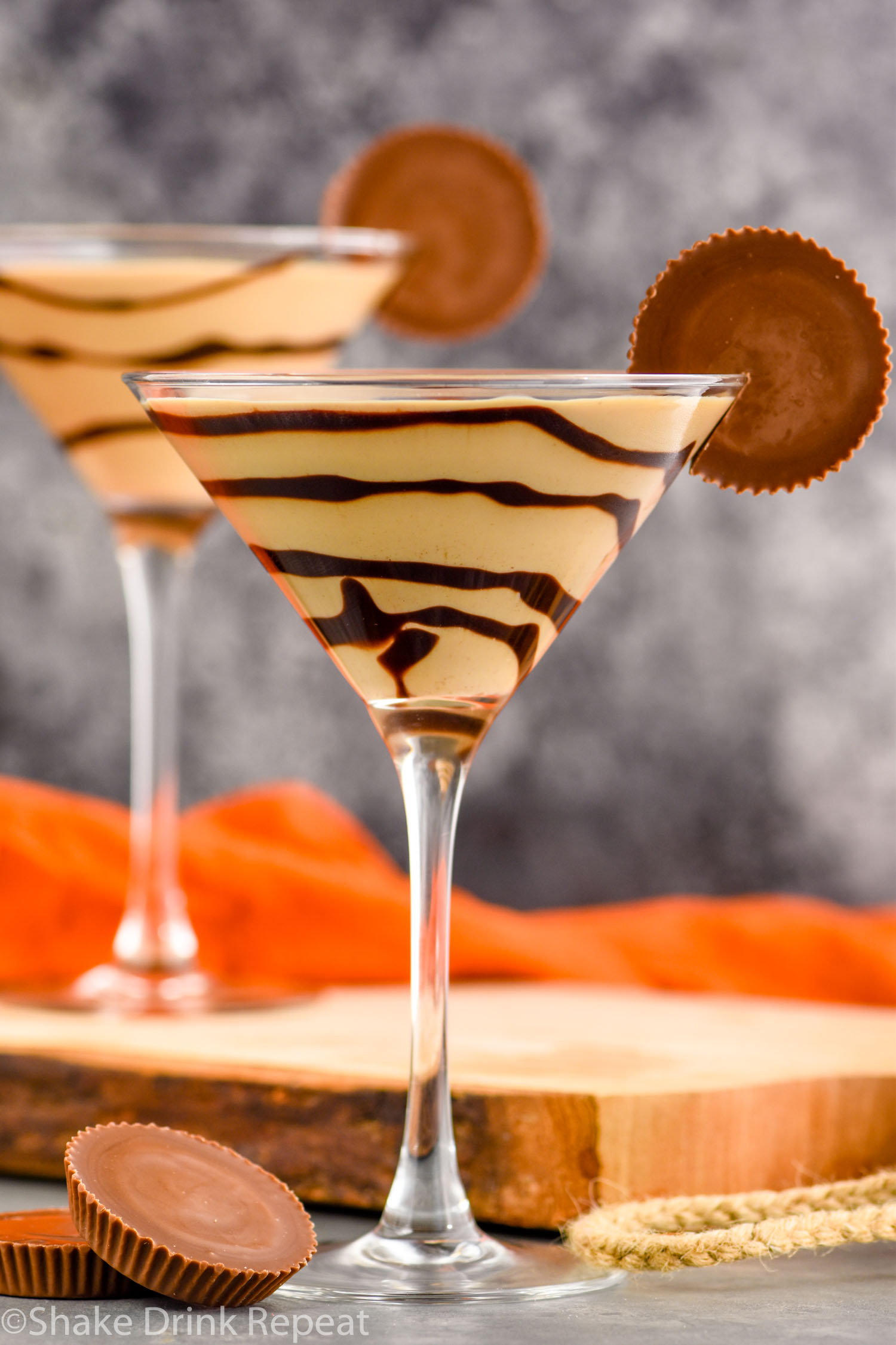 two martini glasses of Peanut Butter Cup Martini recipe garnished with chocolate drizzle and a peanut butter cup.