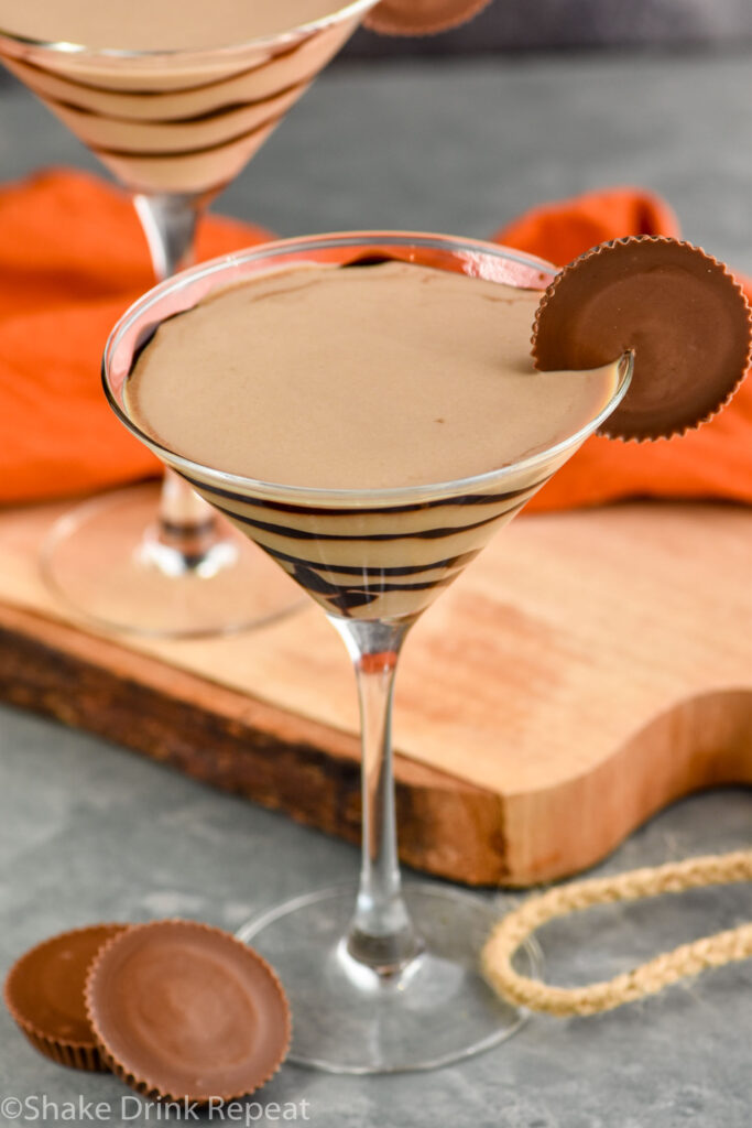 two martini glasses of Peanut Butter Cup Martini recipe garnished with chocolate drizzle and a peanut butter cup.