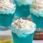 four shot glasses of Blue Scooby Snack Shot topped with whipped cream