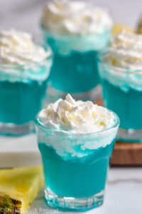 four shot glasses of Blue Scooby Snack Shot topped with whipped cream