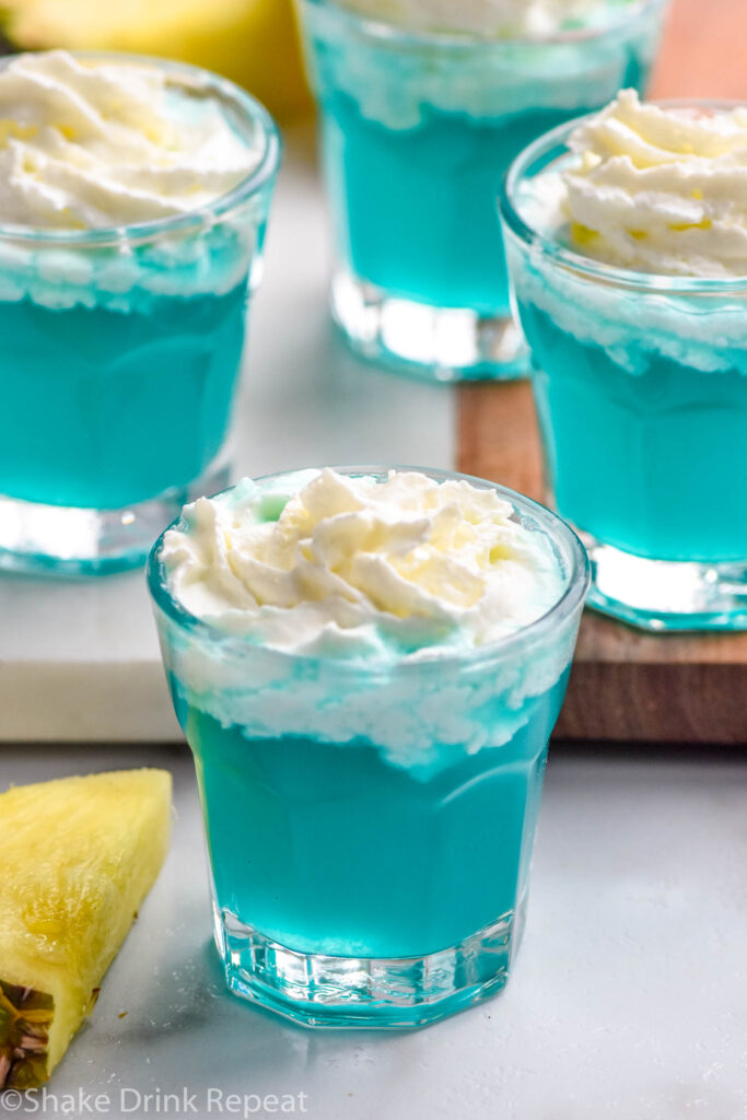 four shot glasses of Blue Scooby Snack Shot topped with whipped cream