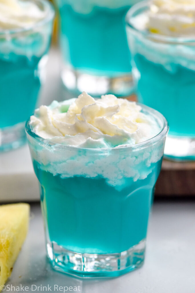 four shot glasses of Blue Scooby Snack Shot topped with whipped cream