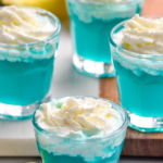 four shot glasses of Blue Scooby Snack Shot topped with whipped cream