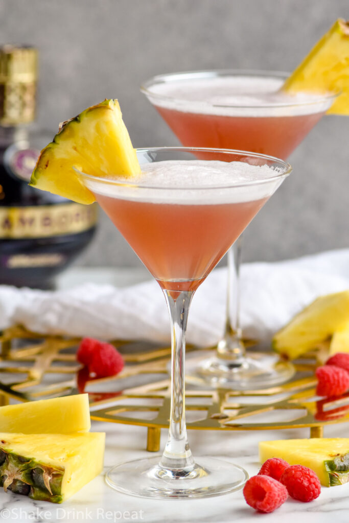 two glasses of French Martini garnished with fresh pineapple, surrounded by raspberries and fresh pineapple