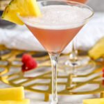 two glasses of French Martini garnished with fresh pineapple, surrounded by raspberries and fresh pineapple