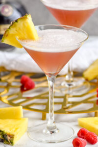 two glasses of French Martini garnished with fresh pineapple, surrounded by raspberries and fresh pineapple