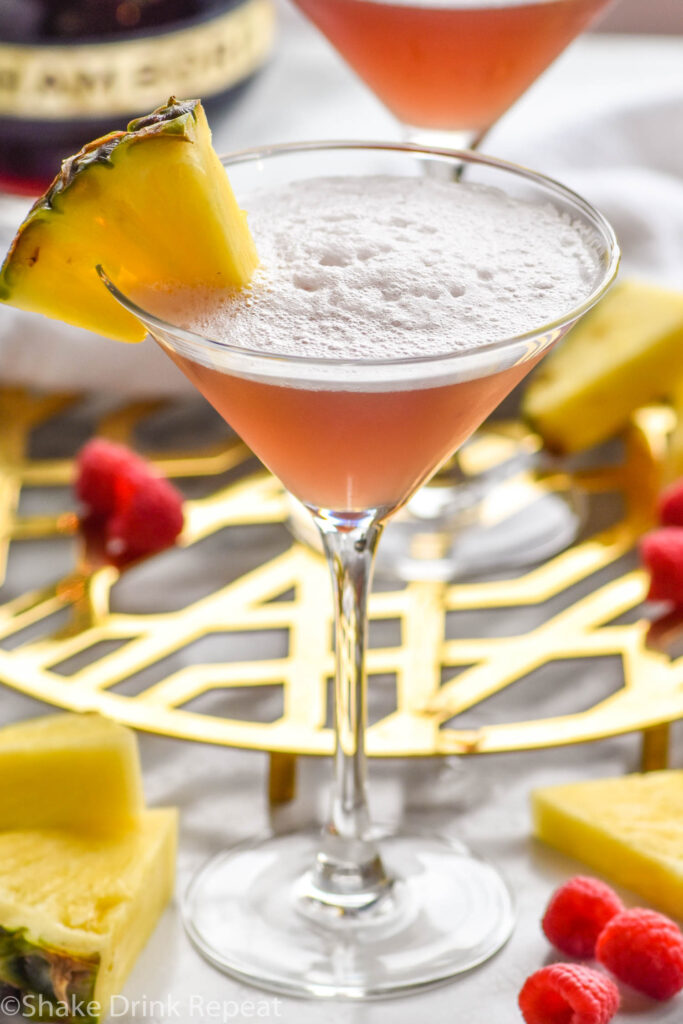 Martini glass of French Martini garnished with fresh pineapple, surrounded by raspberries and fresh pineapple