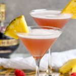 two glasses of French Martini garnished with fresh pineapple, surrounded by raspberries and fresh pineapple