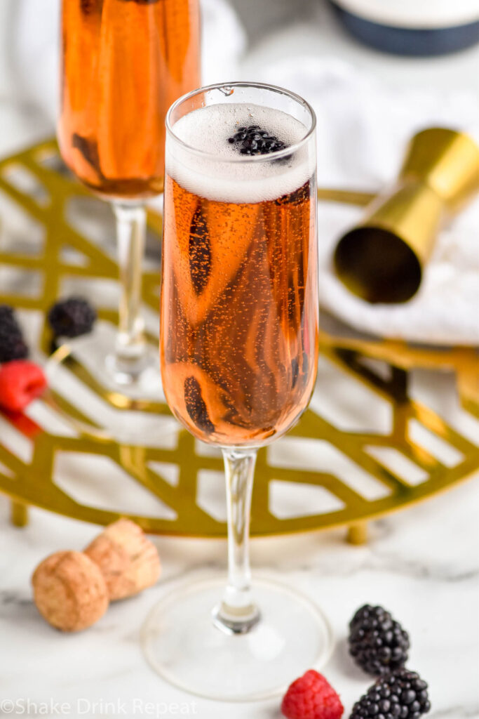 two champagne flutes of Kir Royale cocktail surrounded by fresh raspberries and blackberries