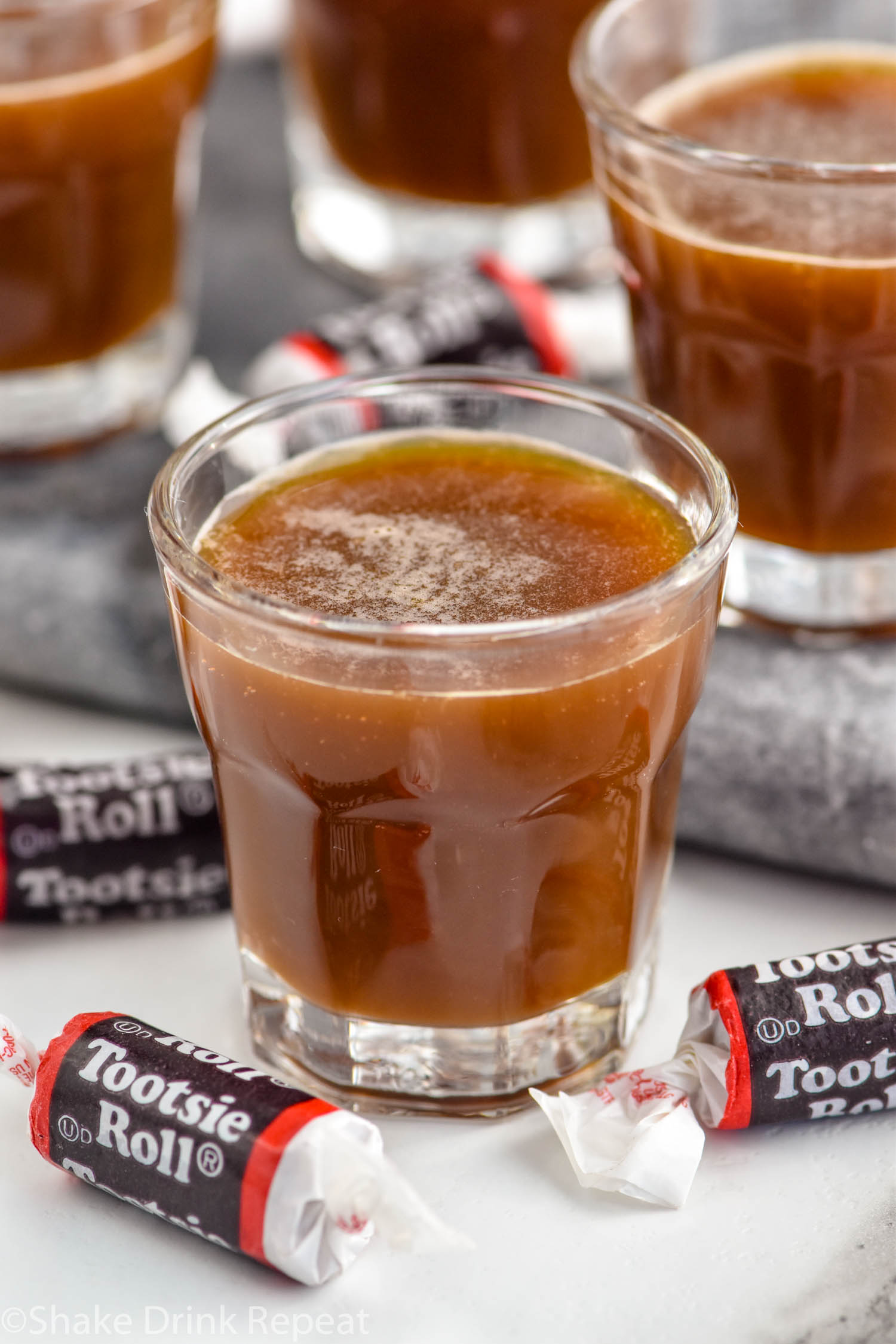 Shot glasses of Tootsie Roll Shot recipe surrounded by Tootsie Roll candies