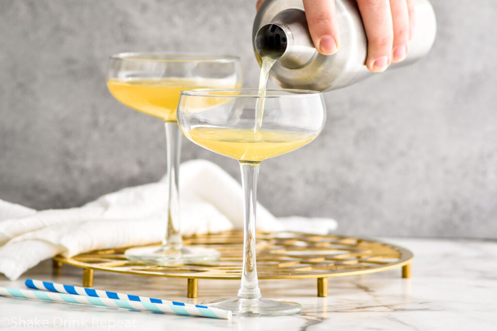 man's hand pouring cocktail shaker of banana daiquiri ingredients into a glass