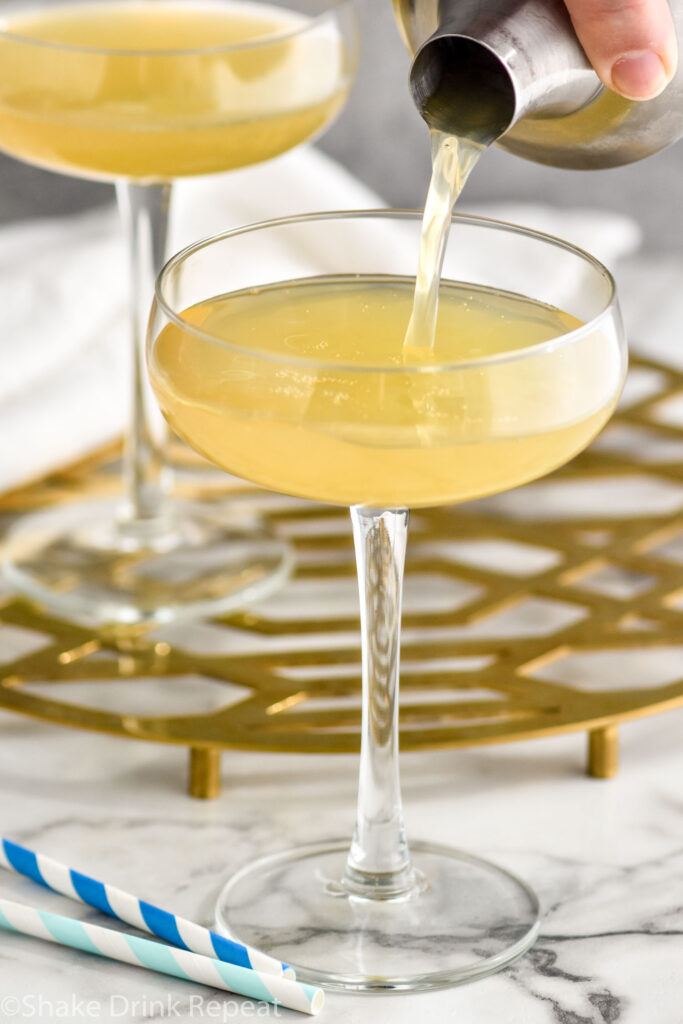 man's hand pouring cocktail shaker of banana daiquiri ingredients into a glass