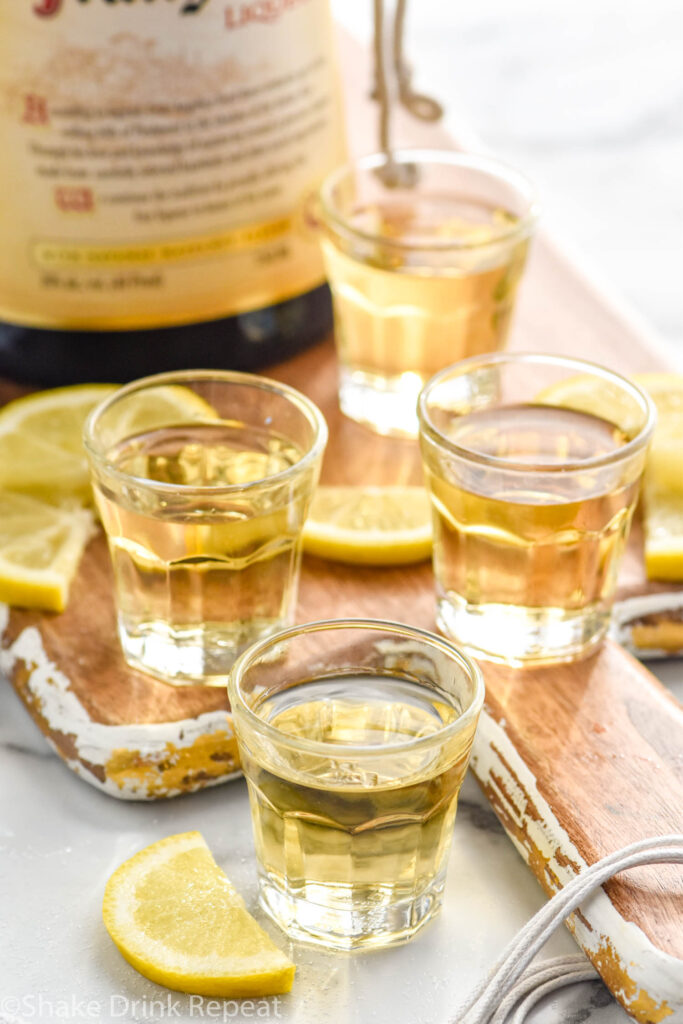 four shot glasses of chocolate cake shot recipe surrounded by lemons and a bottle of Hazelnut liqueur