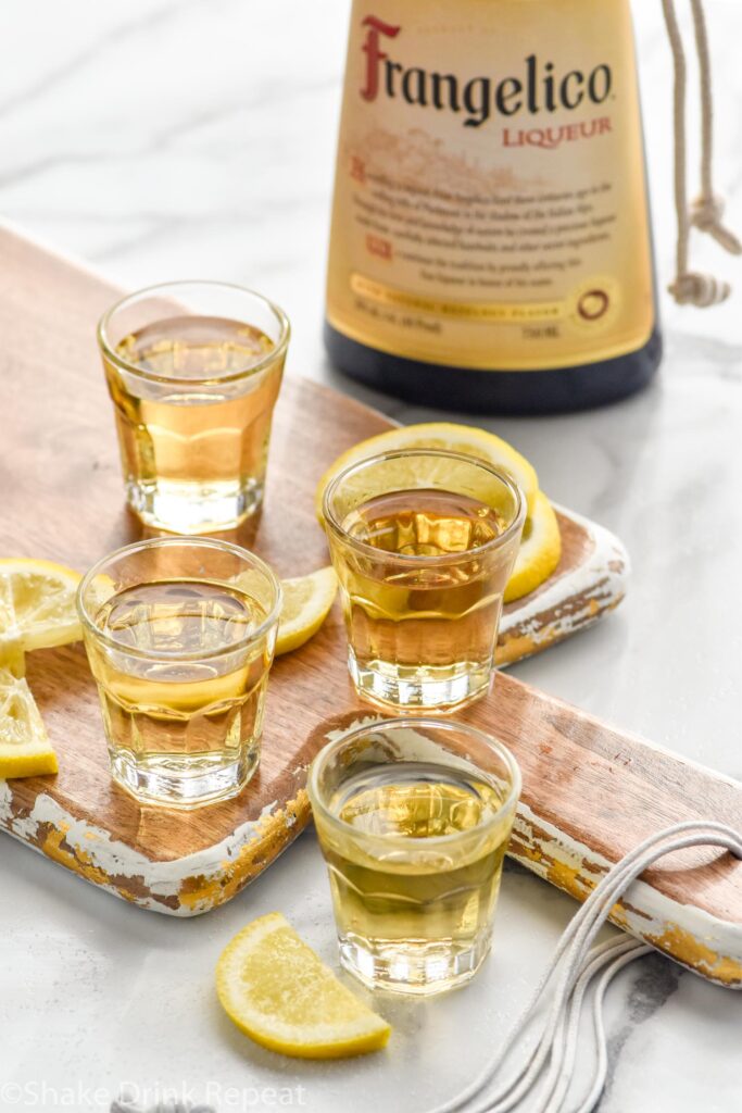 four shot glasses of chocolate cake shot recipe surrounded by lemons and a bottle of Hazelnut liqueur