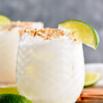 Glass of Coconut Margarita with ice and toasted coconut rim with garnished with lime wedge