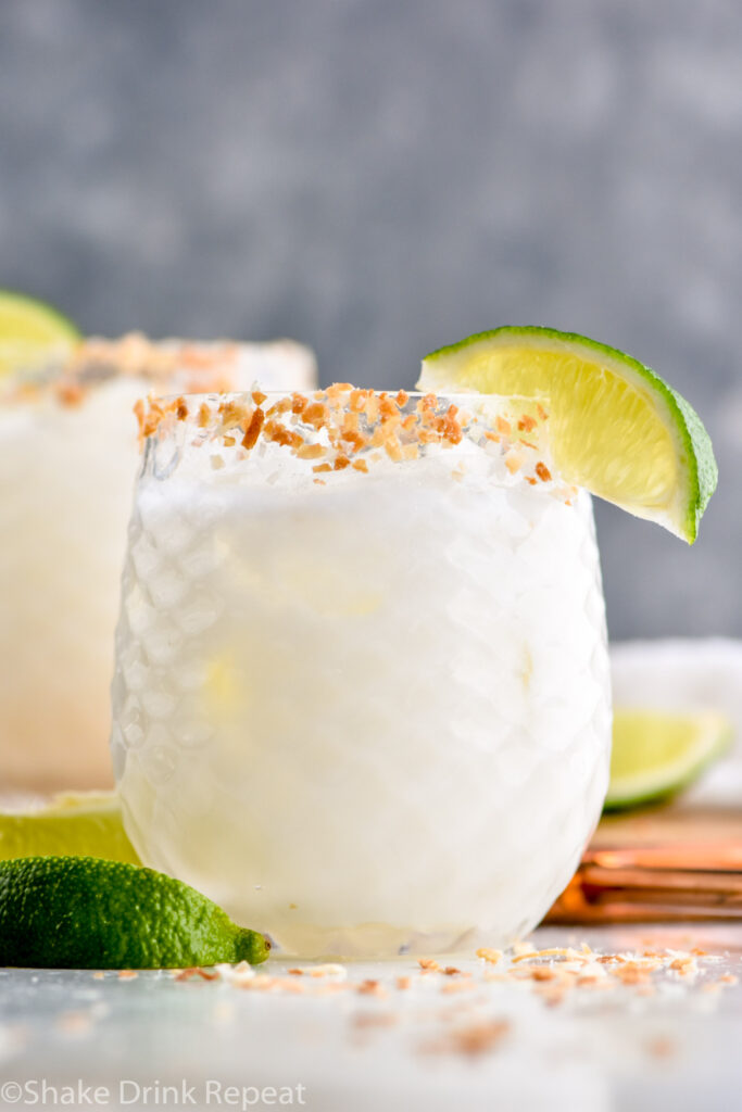 Glass of Coconut Margarita with ice and toasted coconut rim with garnished with lime wedge