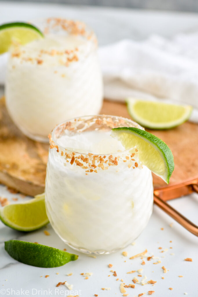 two glasses of Coconut Margarita with ice and toasted coconut rim with garnished with lime wedge