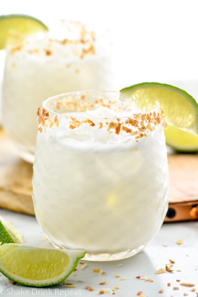Two glasses of Coconut Margarita with ice and toasted coconut rim with garnished with lime wedge