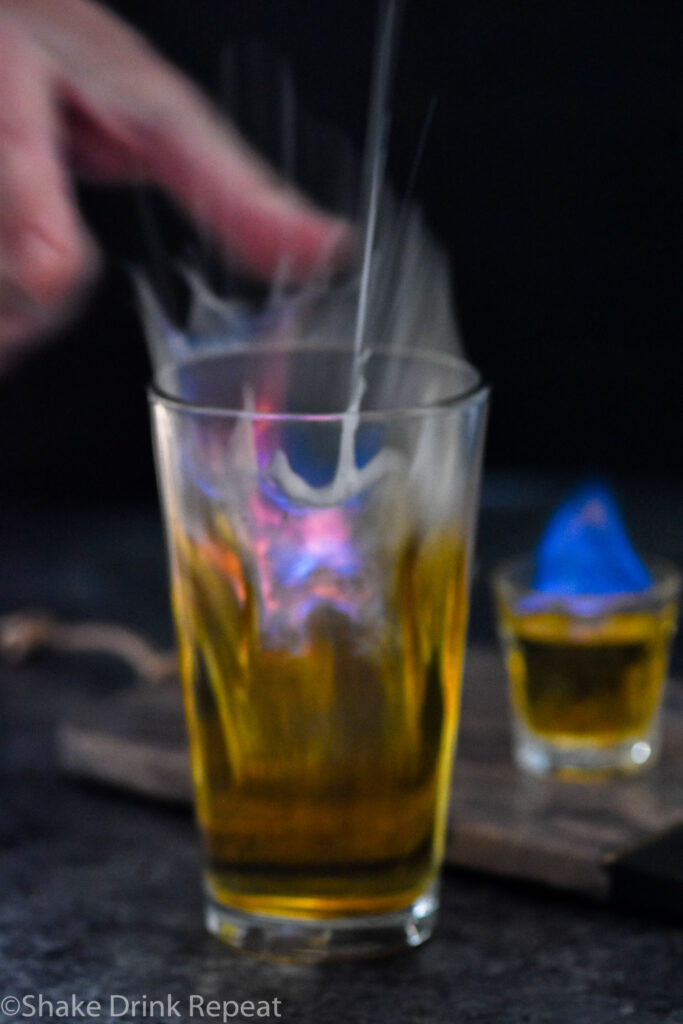 man's hand dropping shot glass of Flaming Dr. Pepper ingredients into a glass of beer