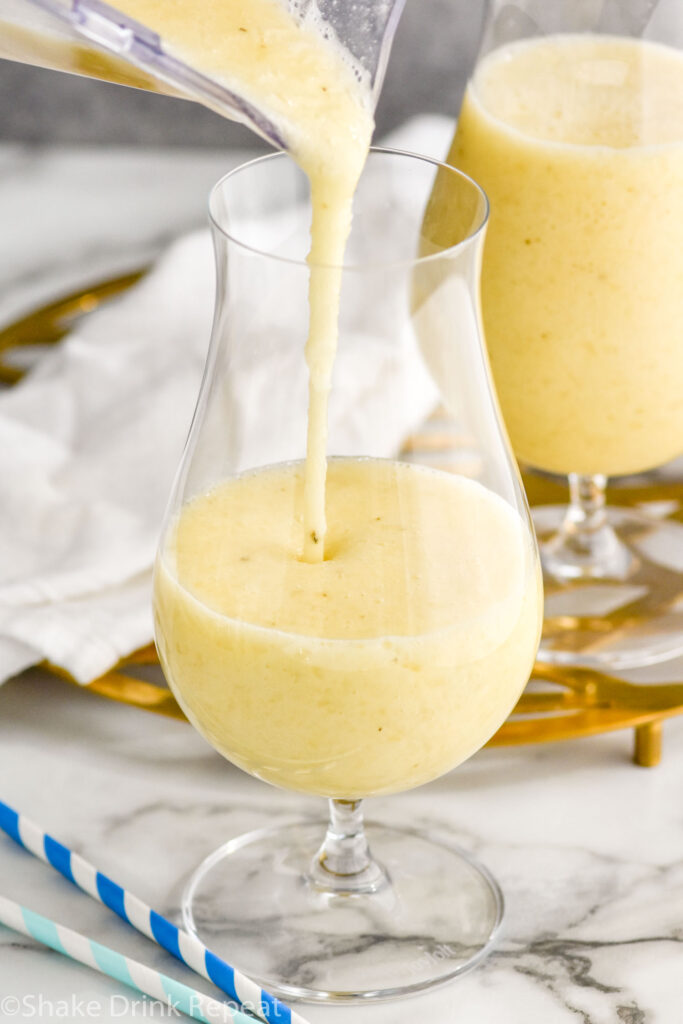 blender of Frozen Banana Daiquiri pouring into a hurricane glass