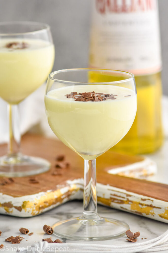 Two glasses of Golden Cadillac recipe garnished with chocolate shavings with bottle of Galliano in the background