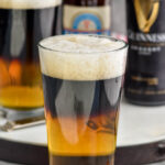 two glasses of black and tan beer with bottles of Guinness and pale ale in the background