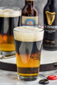 two glasses of black and tan beer with bottles of Guinness and pale ale in the background